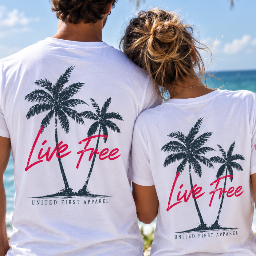 A man and a woman standing on a beach, viewed from behind, wearing matching white t-shirts with a black palm tree graphic and the words 'Live Free' in pink, plus 'UNITED FIRST APPAREL' printed below.
